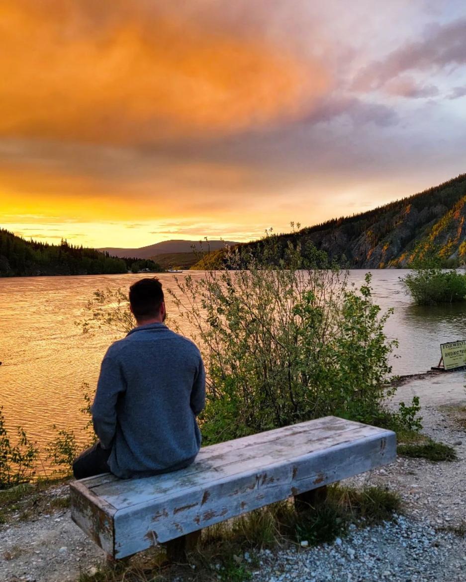 Man sitting on a bench looking at a lake at sunset