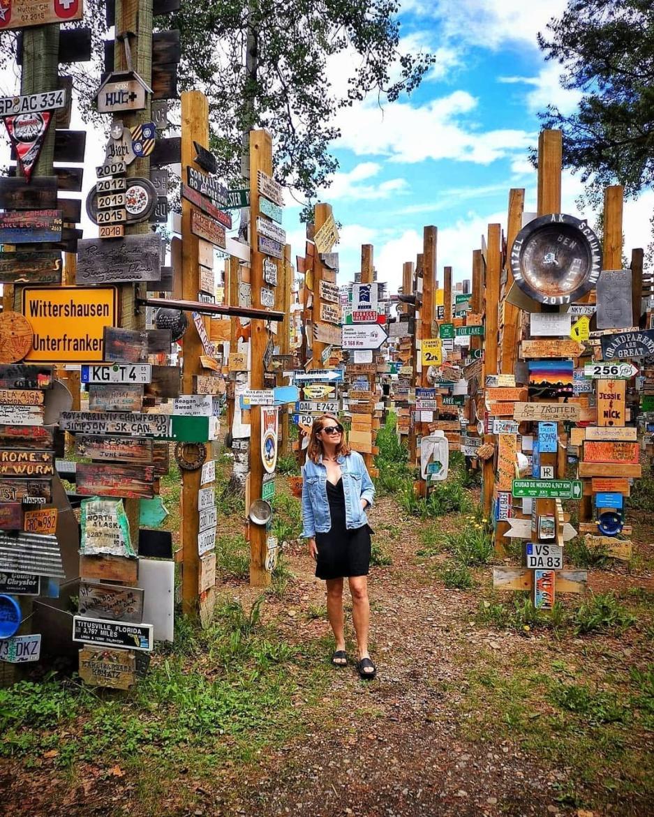 A girl stands amongst a large collection of sign posts