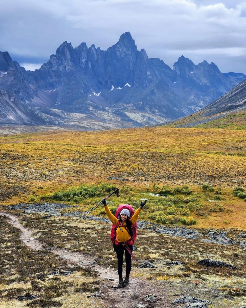 A woman smiles with her hands up in a vest mountain range