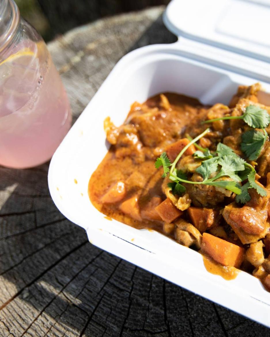 A styrofoam container of food next to a pink drink in a glass mason jar