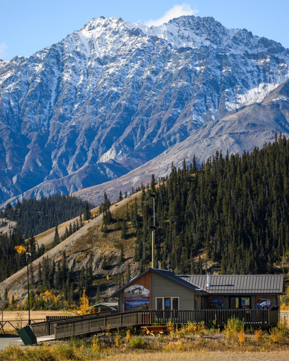 A small green building in front of a large, snowy mountain