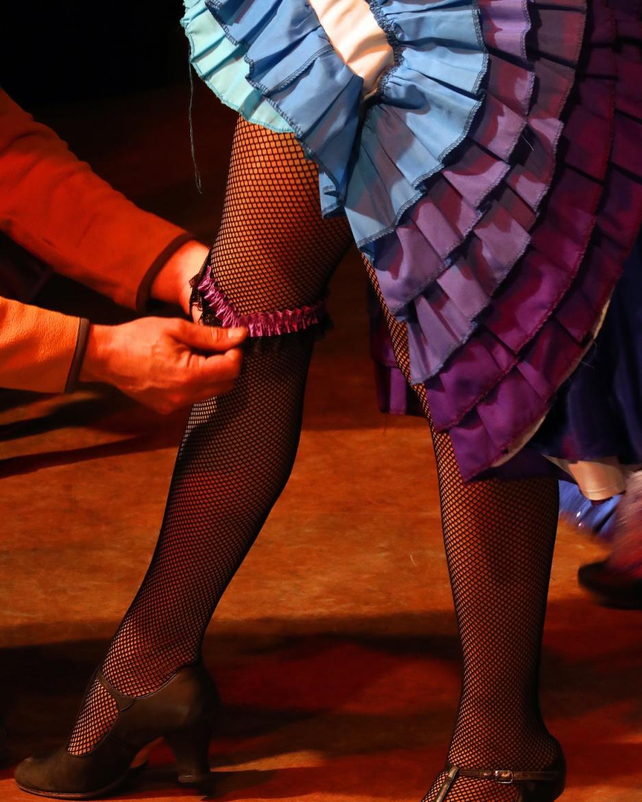 A can can dancer gets a garter put on her leg