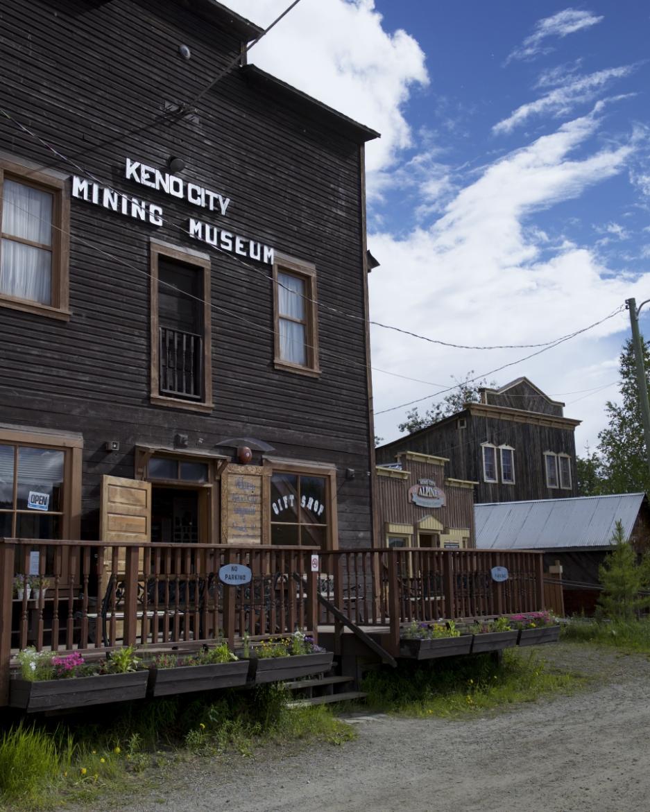 A man stands in front of the Keno City Mining Museum, a two storey dark brown building