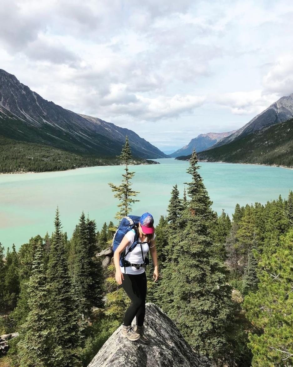 A women hikes over rocks at the end of a bright teal lake