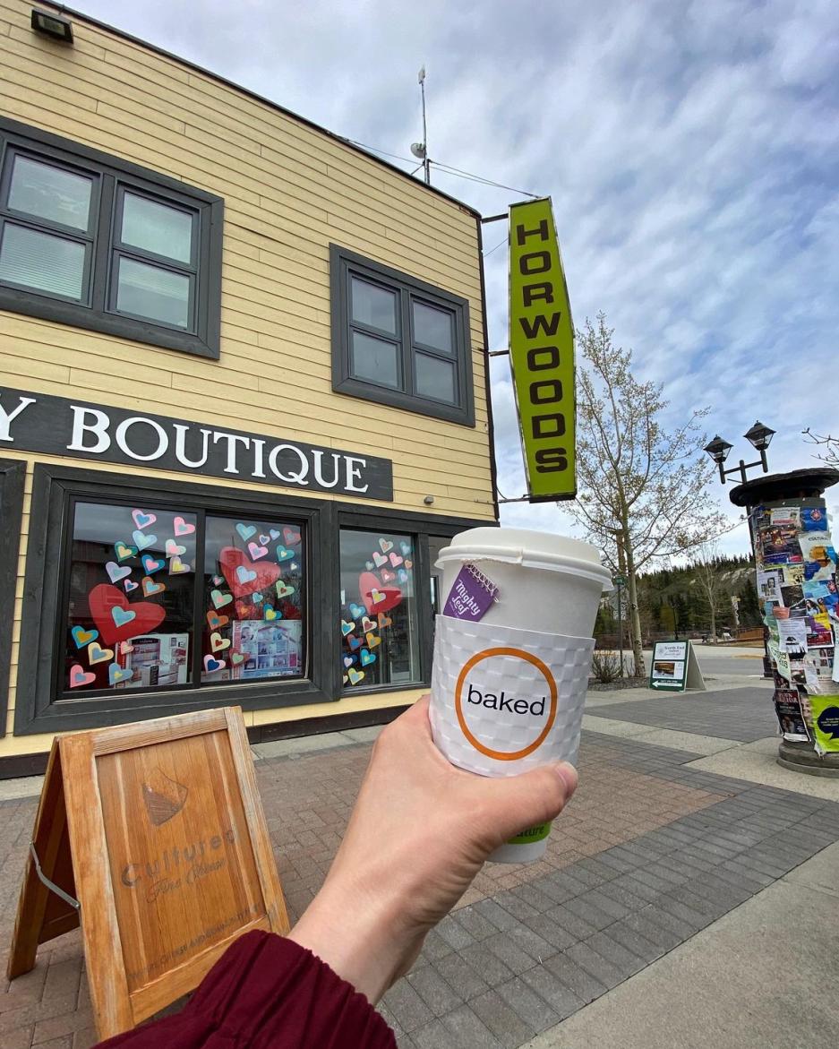 POV style photo of a person holding a coffee cup in front of corner shops downtown
