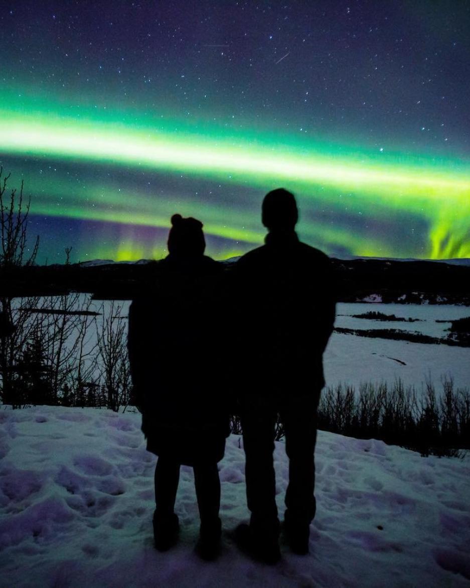 Two people stand watching the northern lights