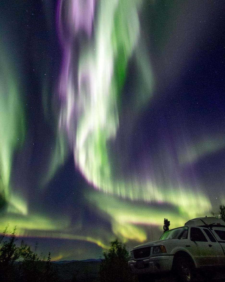 Purple, green and white northern lights swirl above a truck