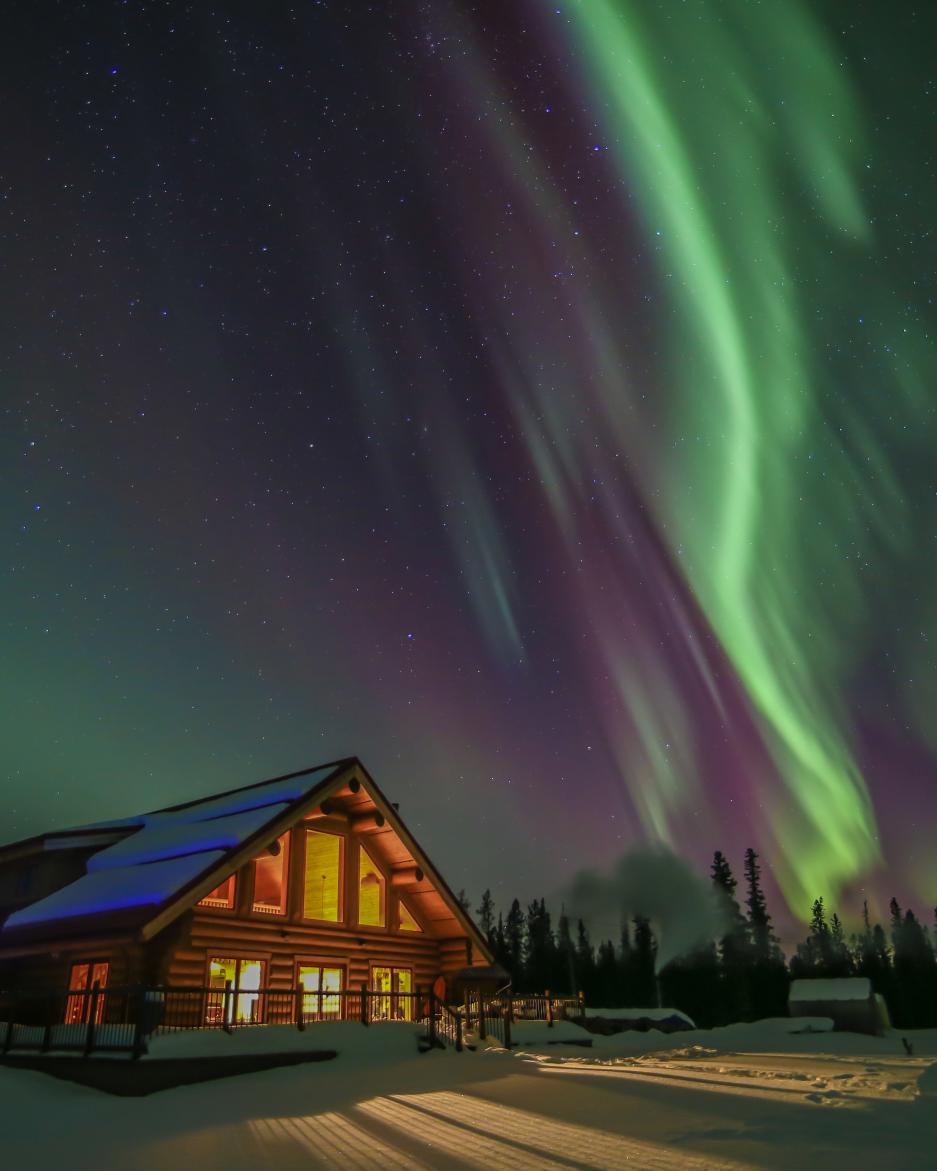 Green and purple northern lights above a wood lodge in the winter