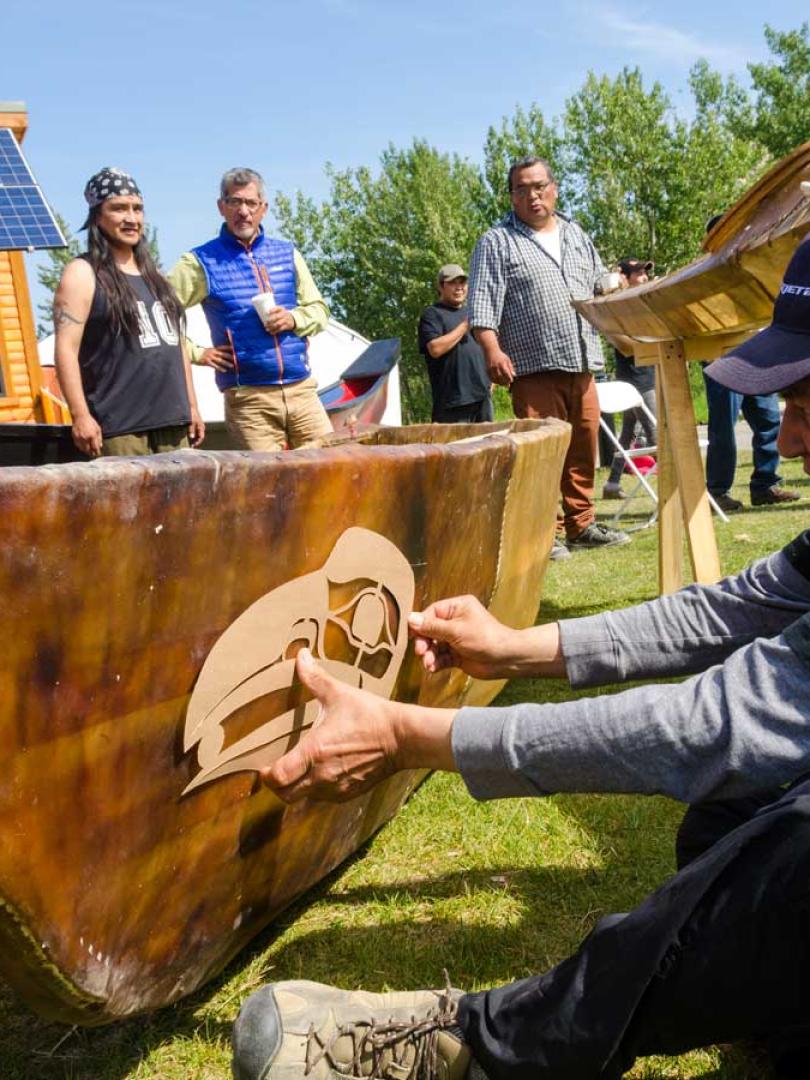 A man stencils a first nations drawing onto a canoe at Adaka Cultural Fest