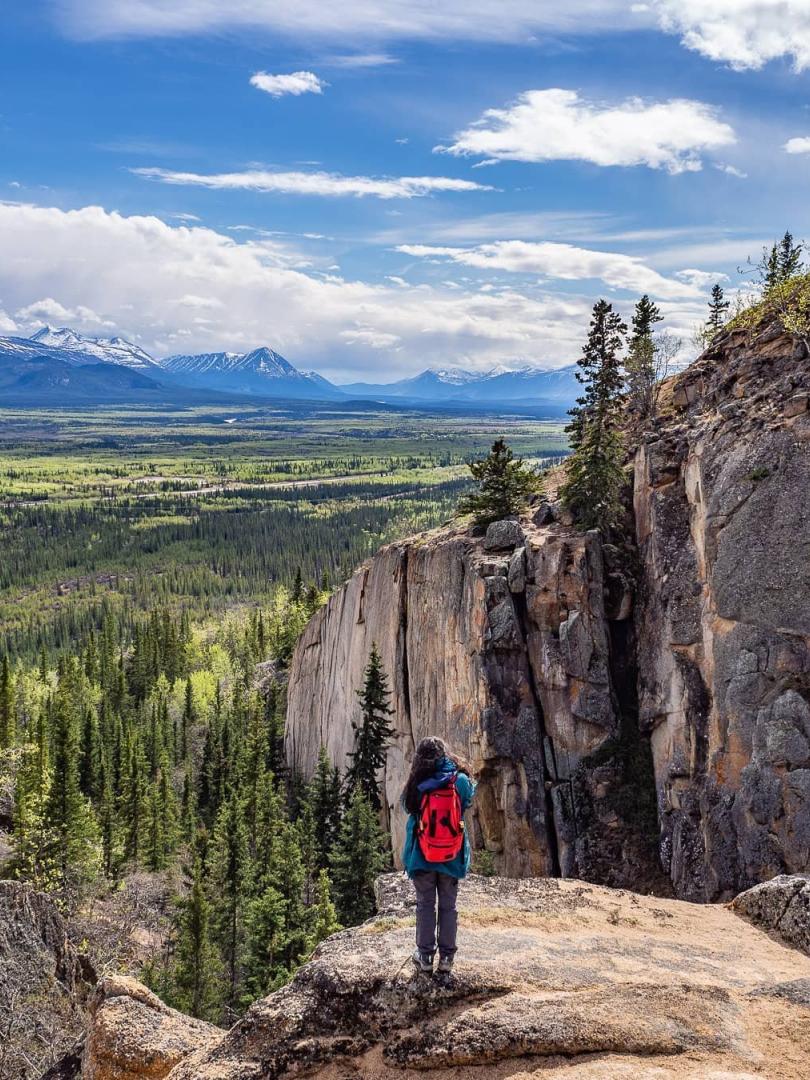 A woman stands with a red backpack overlooking a canyon
