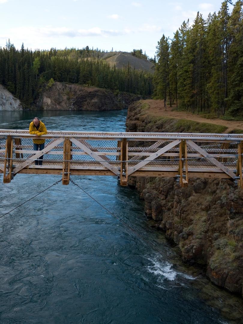 A man stands on a bridge over miles canyon