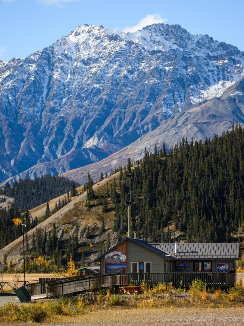 A small green building in front of a large, snowy mountain