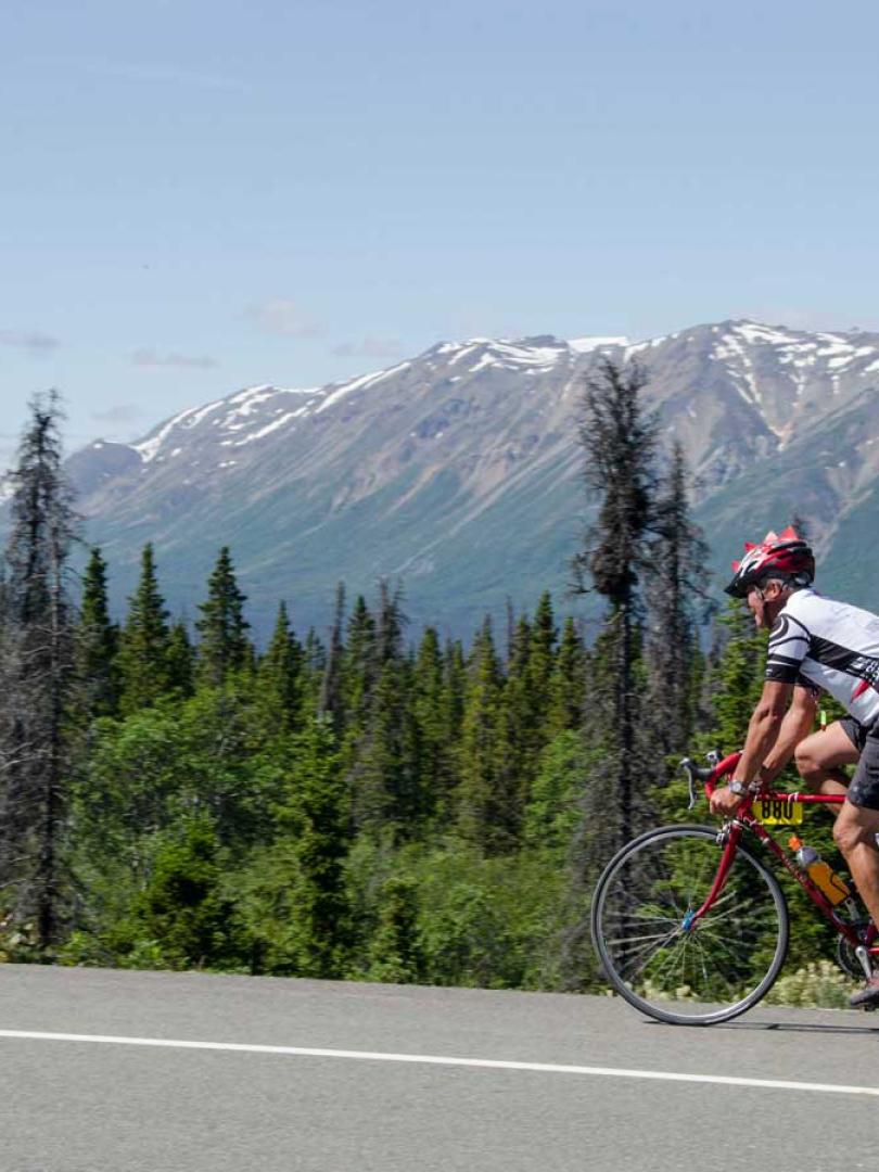 A biker rides on the road with a large mountain in the background. 