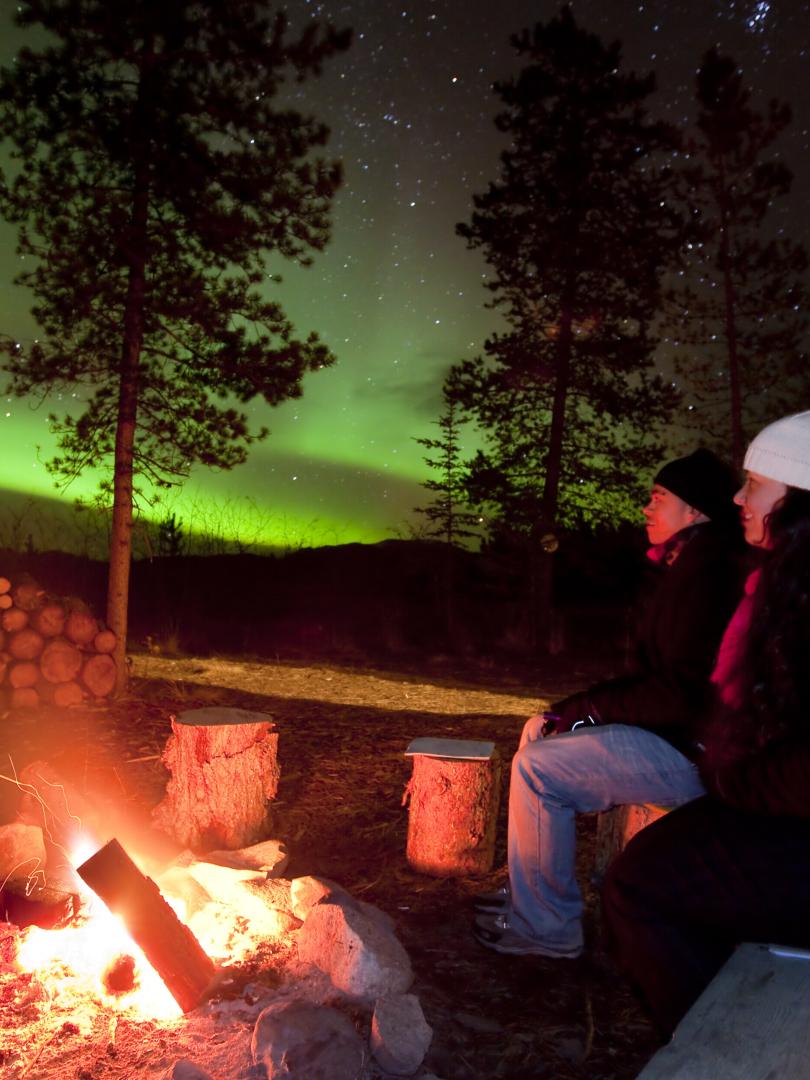 Two people watch the aurora beside a fire
