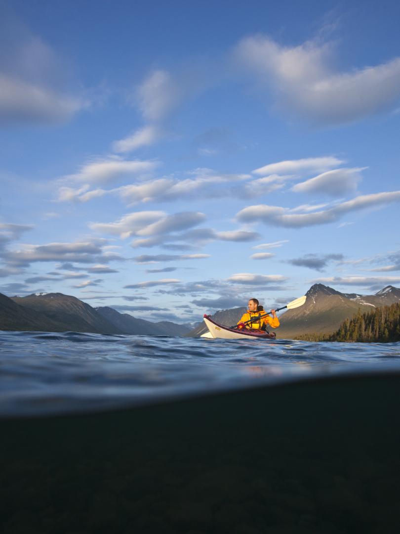 A kayaker paddling on an open lake surrounded by mountains