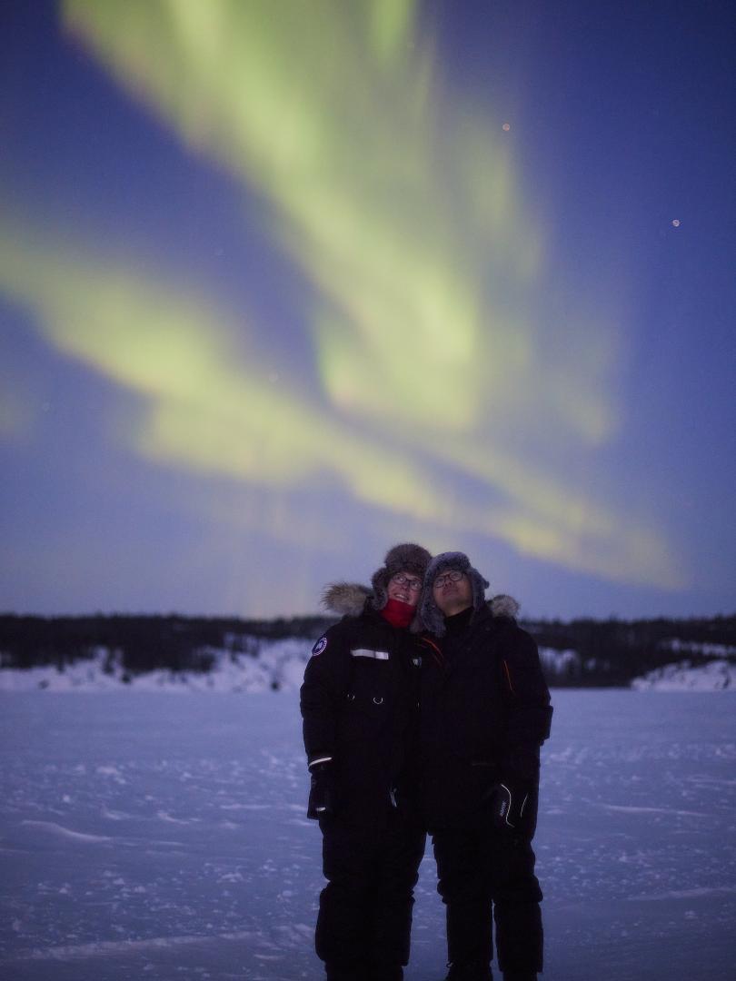 Couple stands together watching the northern lights