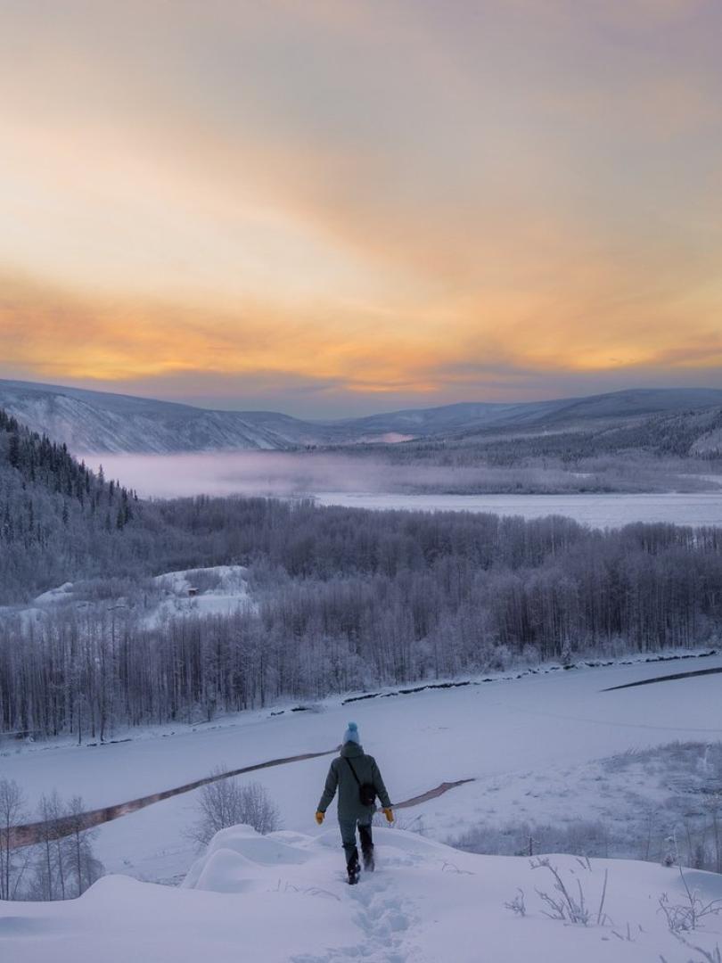 person on a ridge over a snowy river
