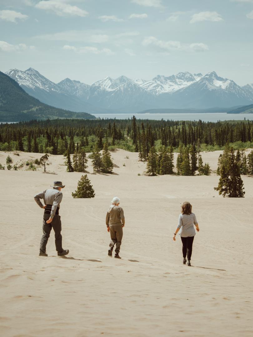 People walking in the desert, with mountains and a lake in the distance
