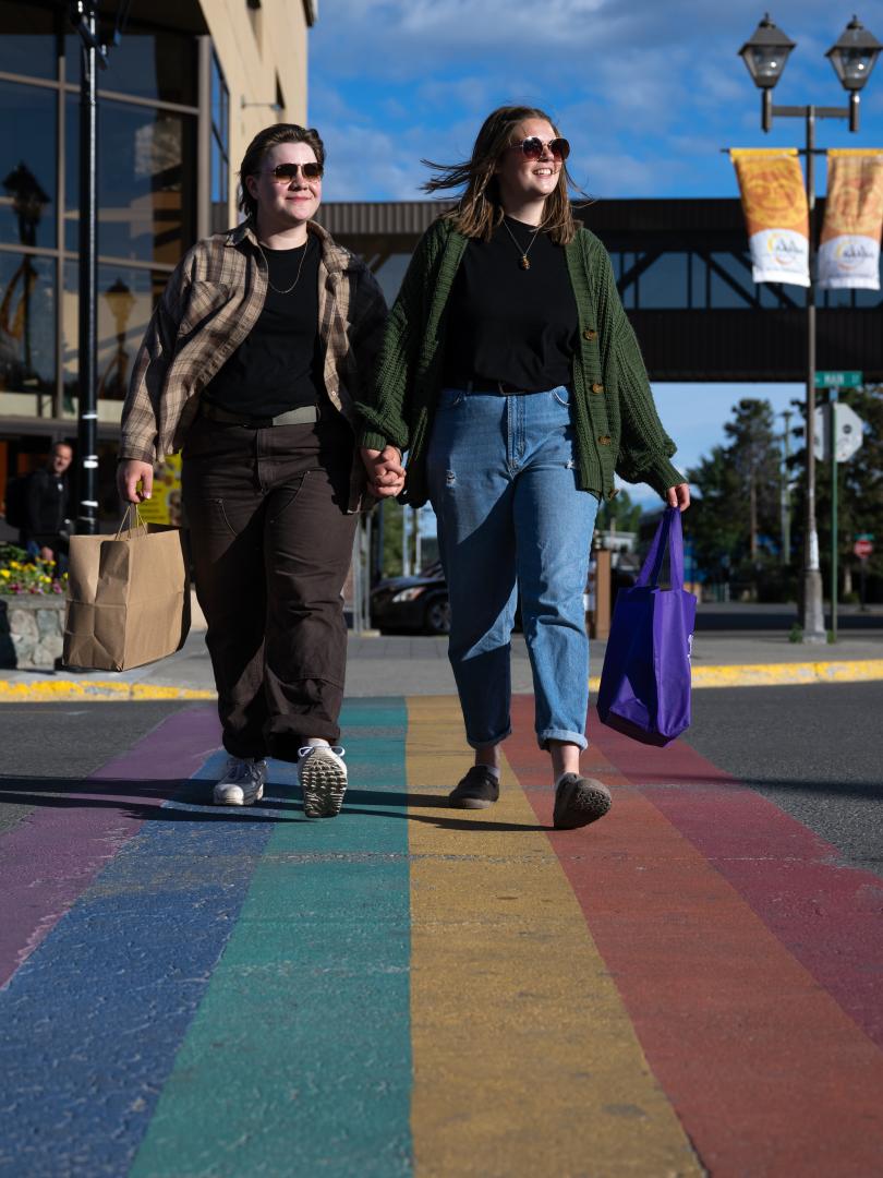 LGBTQ couple shopping, crosses the rainbow crosswalk on Main Street in Whitehorse on a Summer evening.
