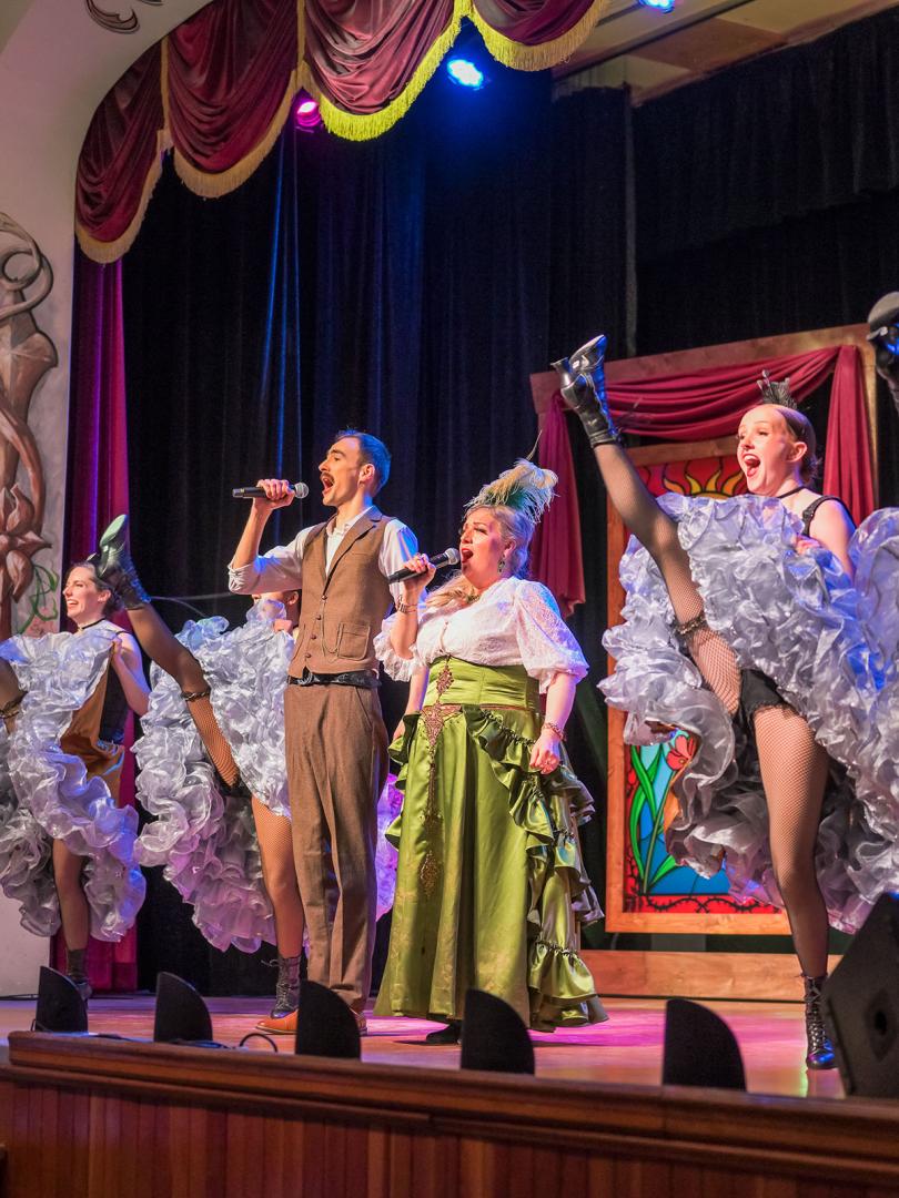 Diamond Tooth Gertie sings and cancan dancers high-kick on the gambling hall stage