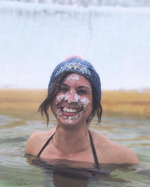A woman in a hot spring smiles with snow on her face