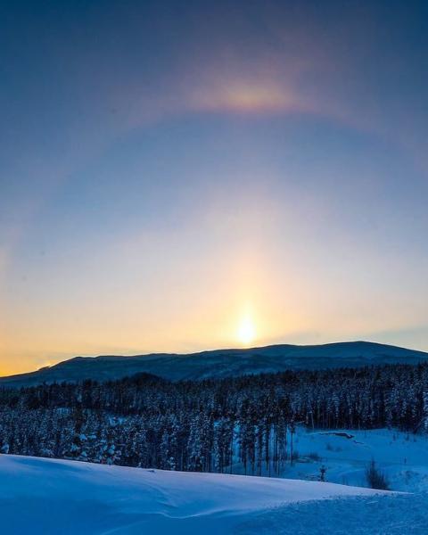 A sundog shines over a mountain along the horizon. The winter sky is dark blue.