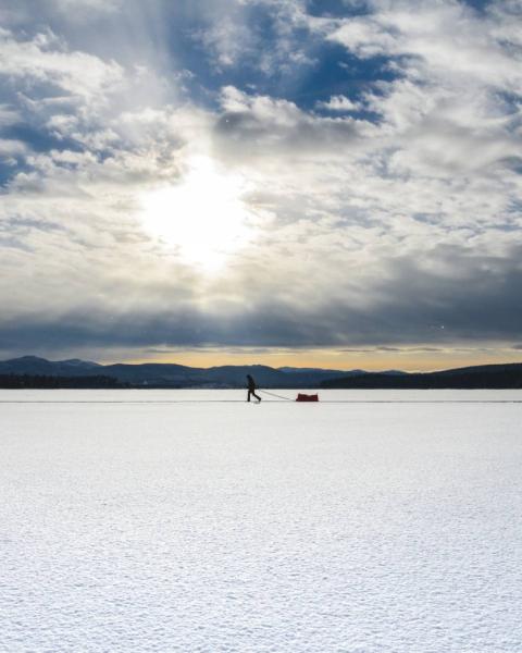 A runner runs across a frozen lake underneath a clouded blue sky.