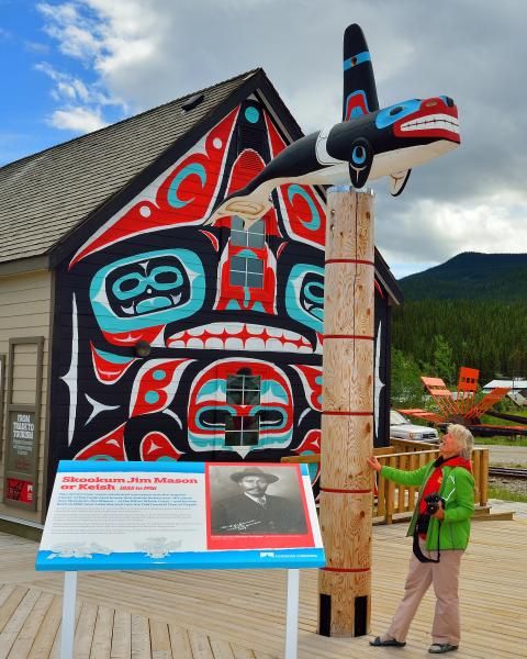 A woman stands in front of a totem pole in carcross