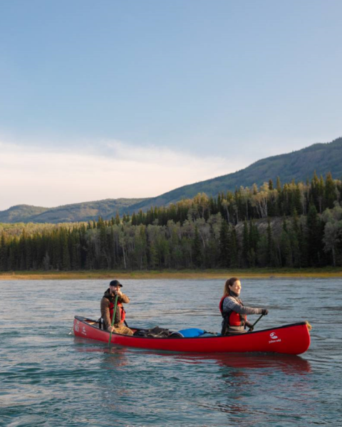 Two people in a red canoe paddle along a river