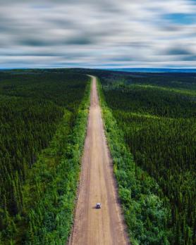 A car on an isolated road is surrounded by vast wilderness