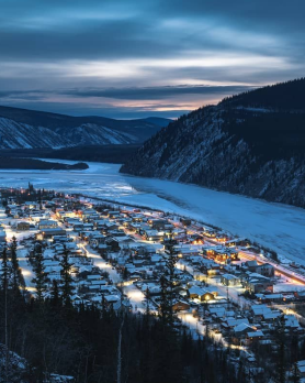 Lights flow from a small town in a mountain valley, next to a large river