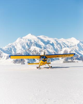 A yellow plane has landed in front of a large, jagged mountain