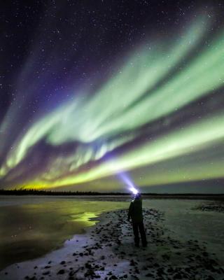 Aurora shines over someone in front of a lake wearing a headlamp