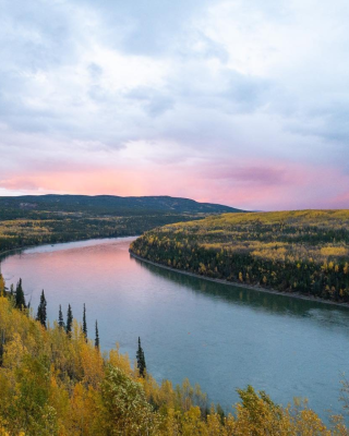The sun sets over a river bend, wrapping around the colours of fall