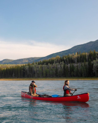 Two people in a red canoe paddle along a river 