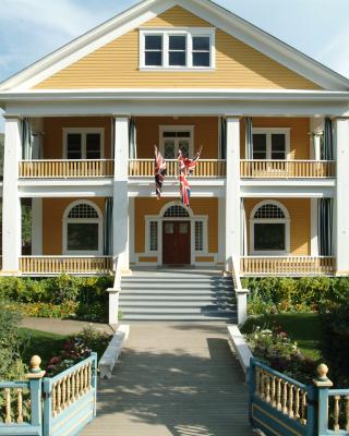 A yellow house with a white picket fence, green front lawn and tall white pillars