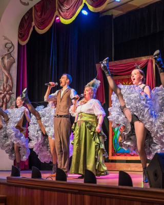 Diamond Tooth Gertie sings and cancan dancers high-kick on the gambling hall stage