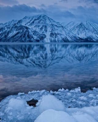 A clear, open lake reflects a moody sky and surrounding snow