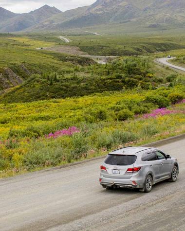 A car driving on the Dempster Highway surrounded by lush rolling hills