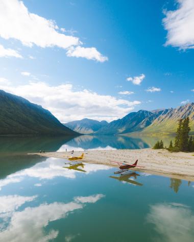Two float planes are docked along the shore of a pristine blue lake