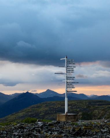 A sign post pointing to cities in many directions stands on a mountaintop