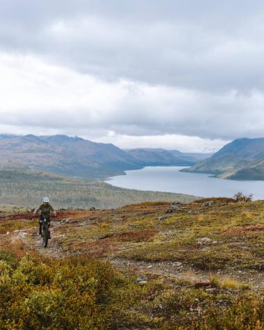 A mountain biker on top of a mountain with a large river and mountain valley behind them