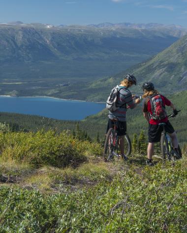 Two people at the top of a mountain biking trail overlooking a bright blue lake