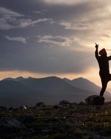 A man dancing on top of a mountain at sunset