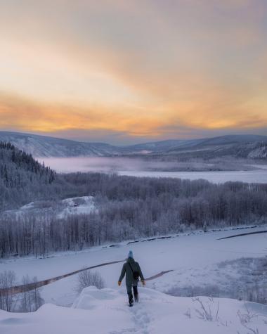person on a ridge over a snowy river