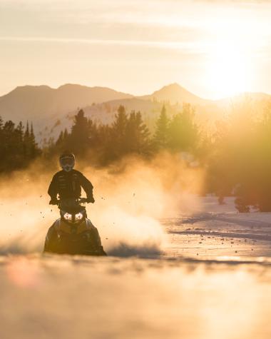 Snowmobiling in golden glow of sunrise