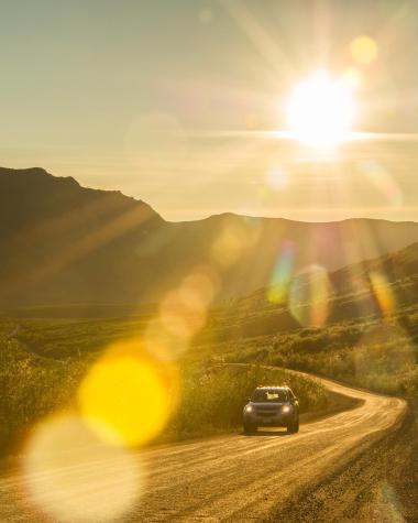 A vehicle goes down the Dempster highway under the midnight sun