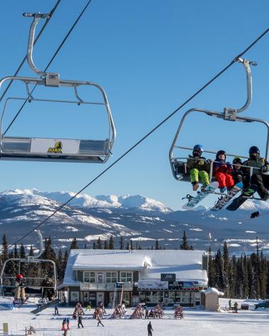 View of the lodge with mountains in the background, and a group of people riding the chairlift.
