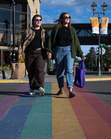 LGBTQ couple shopping, crosses the rainbow crosswalk on Main Street in Whitehorse on a Summer evening.