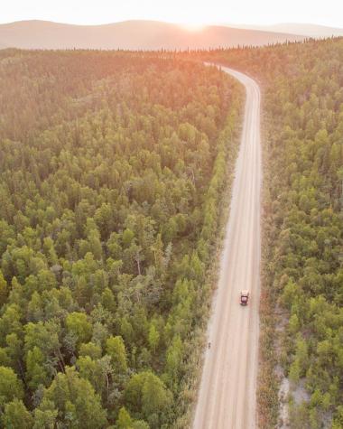 A car drives down a long stretch of highway toward a golden sun